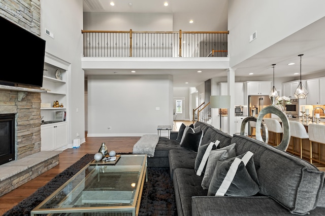 living area with dark wood-style floors, visible vents, a stone fireplace, and baseboards