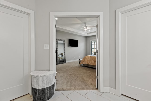 hall with a raised ceiling, light carpet, and baseboards