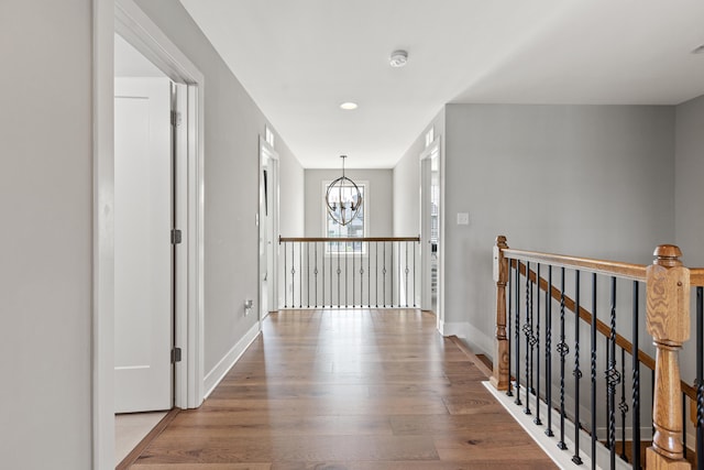 hallway featuring an upstairs landing, baseboards, a notable chandelier, and wood finished floors