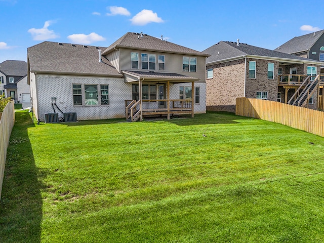 back of property with a shingled roof, a lawn, a fenced backyard, a deck, and brick siding