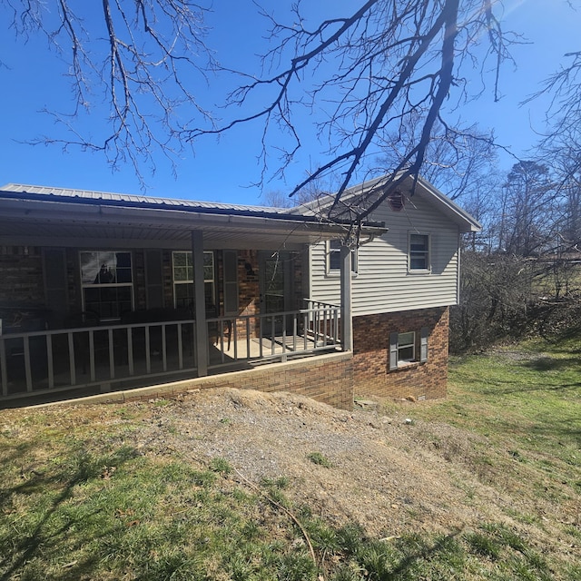 rear view of property featuring metal roof, brick siding, and a sunroom