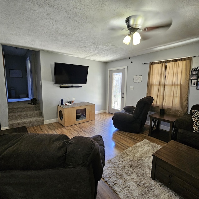 living room with a textured ceiling, wood finished floors, a ceiling fan, baseboards, and stairs