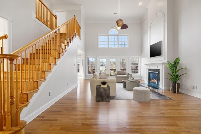 living area featuring a fireplace with flush hearth, wood finished floors, baseboards, and ornamental molding