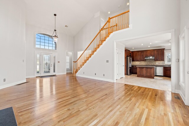 unfurnished living room with stairway, visible vents, baseboards, a towering ceiling, and light wood-type flooring