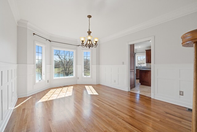 unfurnished dining area with a chandelier, a wainscoted wall, and light wood-style floors