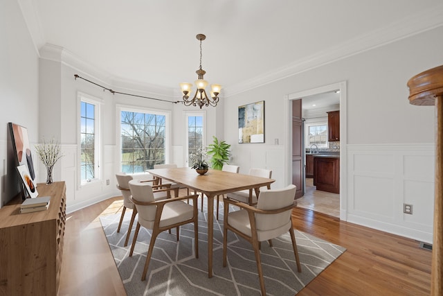 dining space with an inviting chandelier, a healthy amount of sunlight, ornamental molding, and light wood finished floors