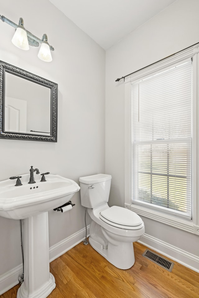 half bath with visible vents, baseboards, and wood finished floors