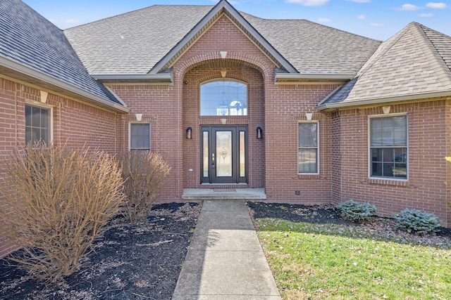 view of exterior entry featuring brick siding and a shingled roof