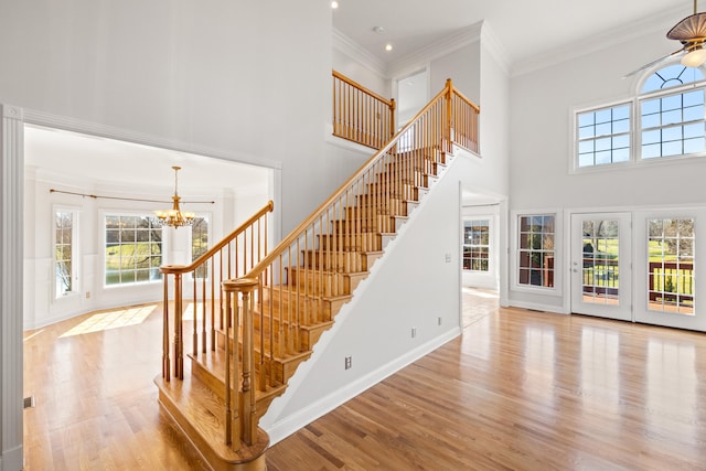 staircase with a high ceiling, an inviting chandelier, wood finished floors, and crown molding