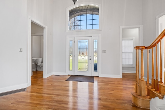 foyer entrance featuring baseboards, stairs, a towering ceiling, and wood finished floors