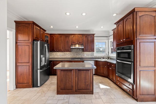 kitchen with dark countertops, backsplash, under cabinet range hood, stainless steel appliances, and a sink