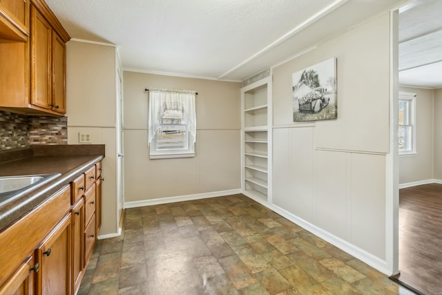 kitchen with a textured ceiling, brown cabinetry, dark countertops, and baseboards