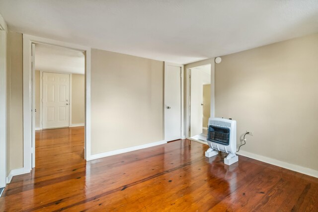 unfurnished living room with heating unit, a wood stove, baseboards, and wood finished floors