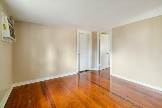 unfurnished room with baseboards, wood finished floors, and an AC wall unit