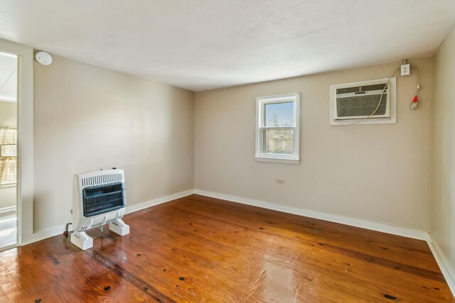 unfurnished living room featuring heating unit, baseboards, an AC wall unit, and wood finished floors