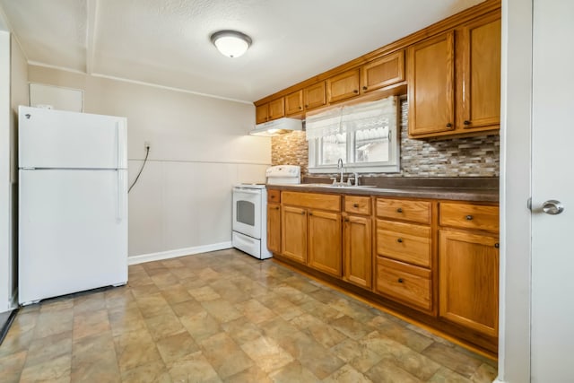 kitchen featuring white appliances, dark countertops, brown cabinets, under cabinet range hood, and a sink