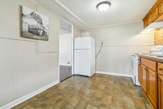 kitchen featuring a decorative wall, brown cabinetry, a textured ceiling, white appliances, and under cabinet range hood