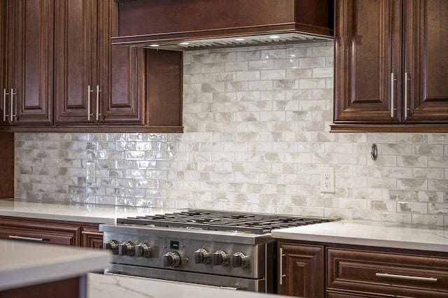 kitchen with light stone counters, decorative backsplash, stove, dark brown cabinets, and premium range hood