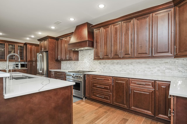 kitchen featuring decorative backsplash, light wood-style flooring, custom range hood, stainless steel appliances, and a sink