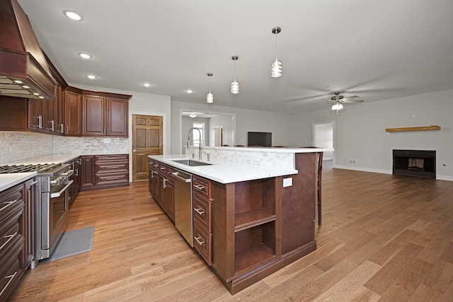 kitchen with stainless steel appliances, a sink, light wood-style floors, open floor plan, and custom exhaust hood