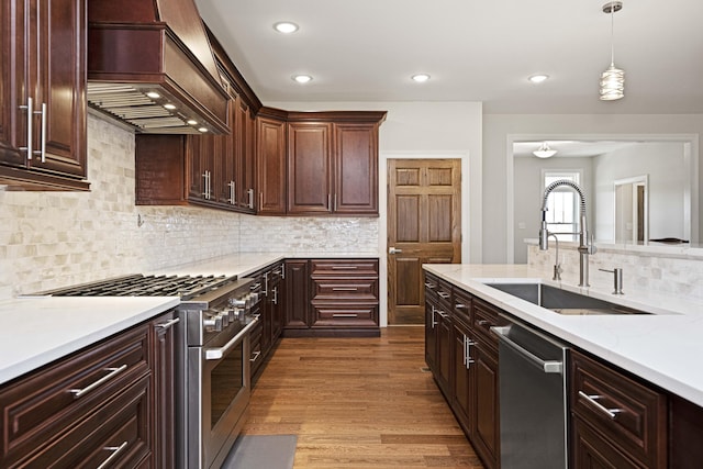 kitchen featuring premium range hood, dark wood-style flooring, a sink, appliances with stainless steel finishes, and pendant lighting