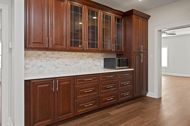 bar featuring dark wood-style flooring, a ceiling fan, baseboards, tasteful backsplash, and stainless steel microwave