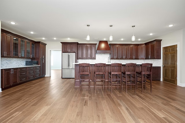 kitchen featuring custom range hood, high quality fridge, light wood-style flooring, and dark brown cabinetry