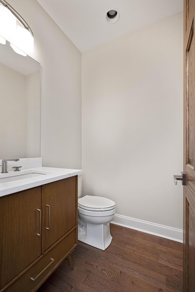 half bath with baseboards, vanity, toilet, and wood finished floors