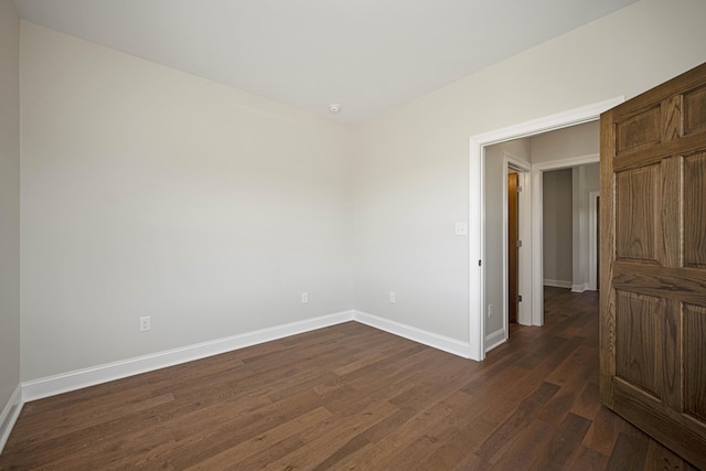 spare room with baseboards and dark wood-type flooring