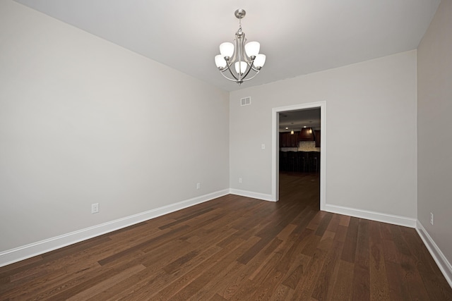 unfurnished room with a notable chandelier, dark wood finished floors, visible vents, and baseboards