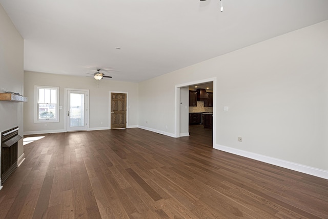 unfurnished living room featuring ceiling fan, a fireplace, baseboards, and dark wood-type flooring