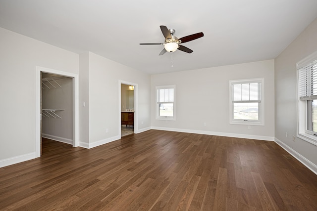 unfurnished bedroom featuring dark wood-type flooring, a walk in closet, ceiling fan, and baseboards