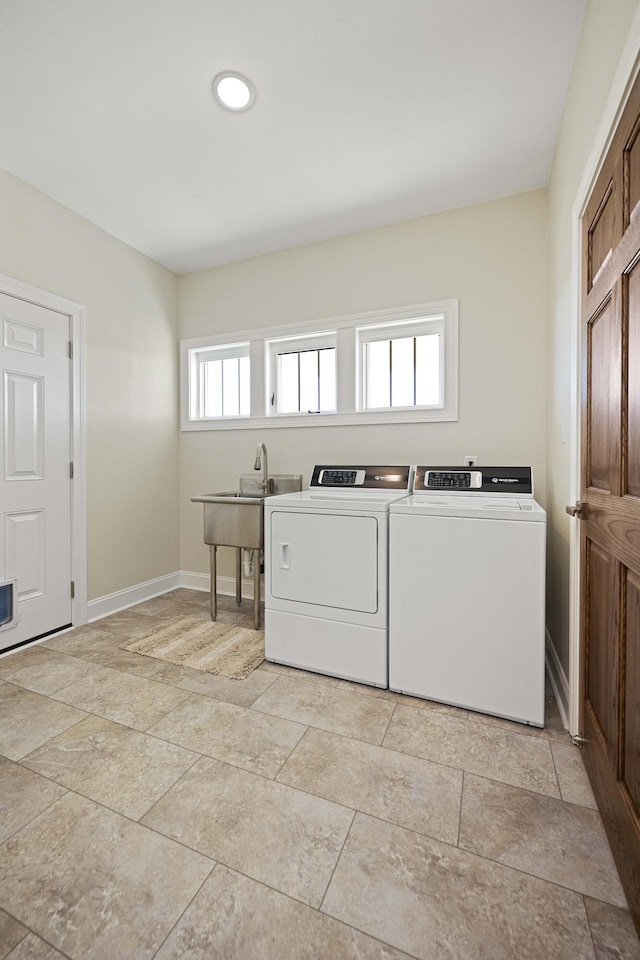 washroom featuring washing machine and dryer, laundry area, a sink, and baseboards