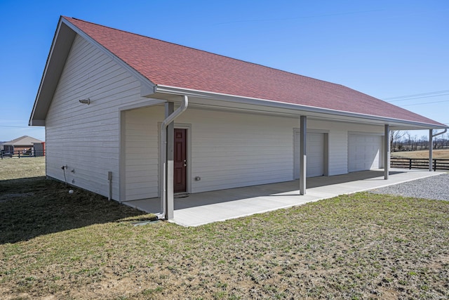 view of property exterior with roof with shingles, a yard, a detached garage, and fence