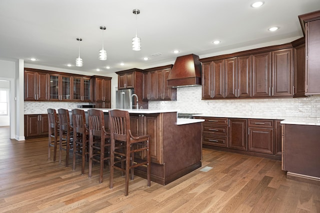 kitchen featuring light wood-style floors, light countertops, premium range hood, and appliances with stainless steel finishes