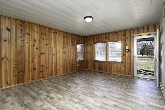 empty room with wooden walls, wood finished floors, and baseboards