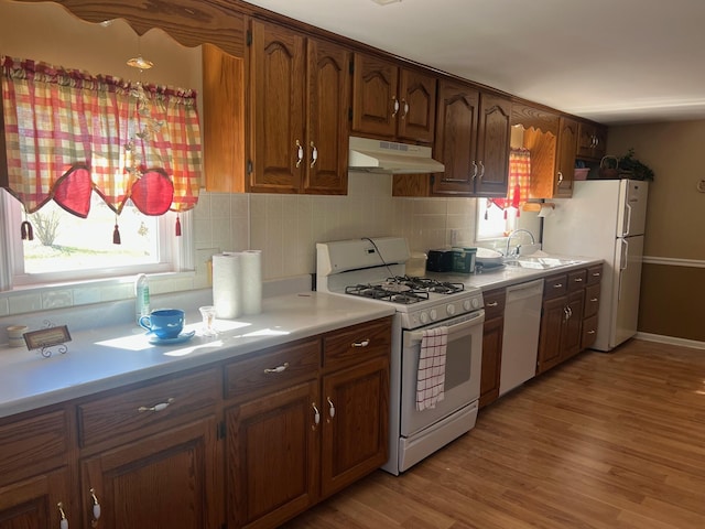 kitchen with white appliances, light countertops, under cabinet range hood, and decorative backsplash