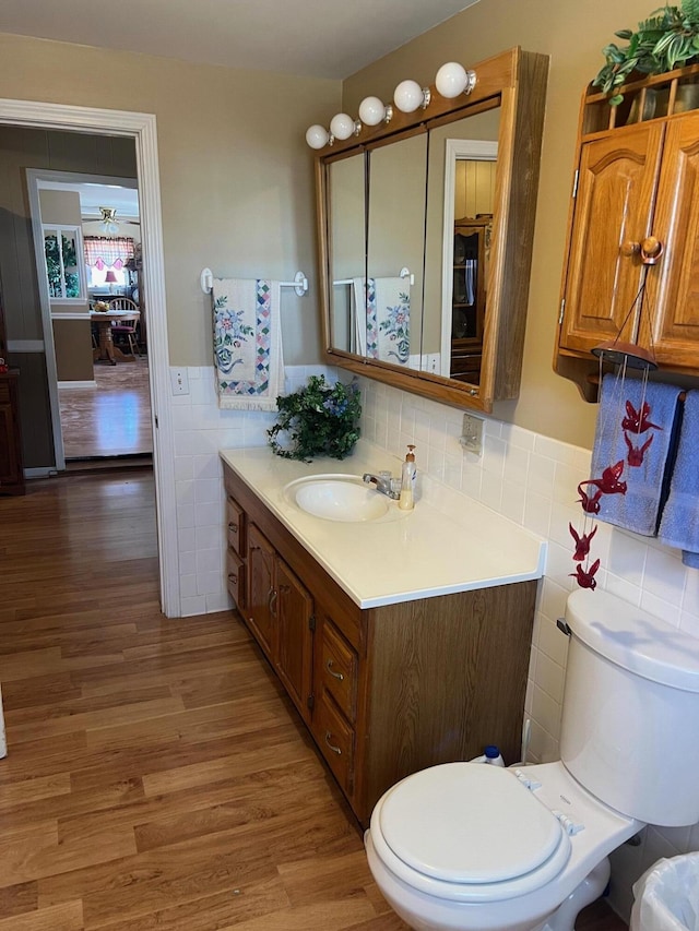 half bathroom featuring a wainscoted wall, tile walls, toilet, vanity, and wood finished floors