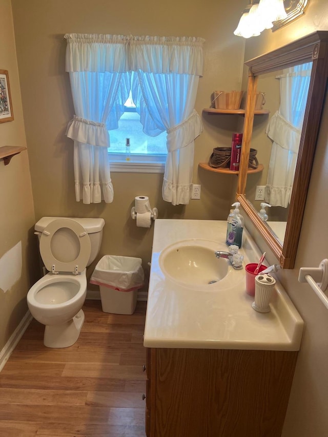 half bath featuring baseboards, vanity, toilet, and wood finished floors