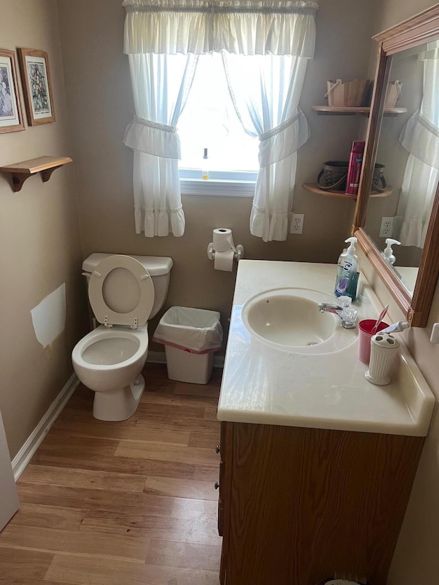 half bath with vanity, wood finished floors, toilet, and baseboards