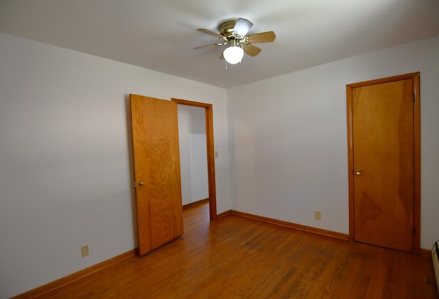 unfurnished room featuring a ceiling fan, a baseboard heating unit, baseboards, and wood finished floors