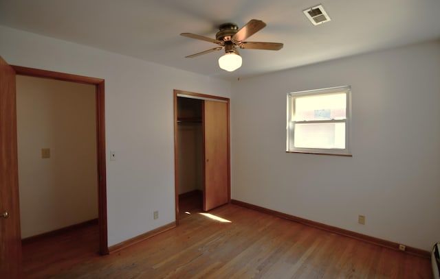 unfurnished bedroom with a closet, visible vents, ceiling fan, wood finished floors, and baseboards