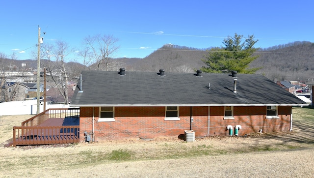 rear view of house featuring a deck, brick siding, and roof with shingles