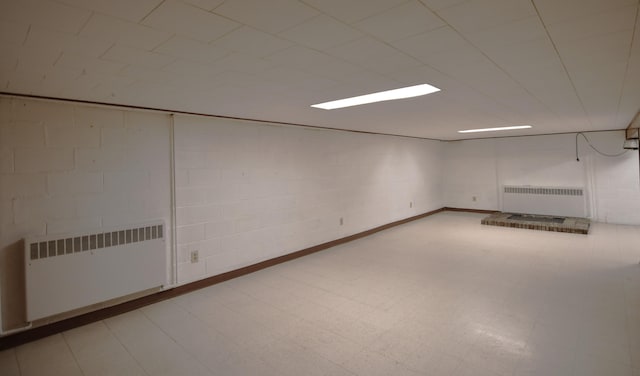 finished basement featuring concrete block wall, light floors, and radiator heating unit