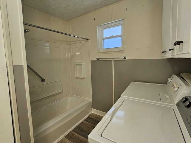 bathroom with a textured ceiling,  shower combination, washer and clothes dryer, and wood finished floors