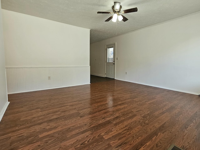 spare room with dark wood-style floors, ceiling fan, a textured ceiling, and a wainscoted wall