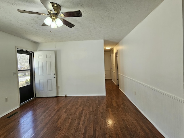 spare room featuring a textured ceiling, ceiling fan, a wainscoted wall, wood finished floors, and visible vents