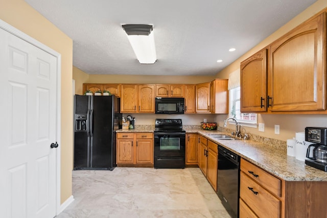 kitchen with brown cabinetry, light stone counters, a textured ceiling, black appliances, and a sink