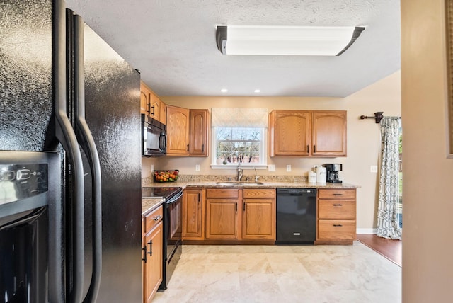 kitchen with brown cabinets, a sink, a textured ceiling, light stone countertops, and black appliances