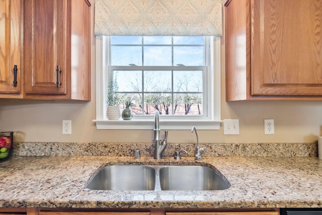 kitchen featuring light stone counters, brown cabinetry, and a sink